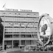 kilkukondygnacyjny przeszklony budynek z napisem na dachu Centrum Targowe, z prawej ażurowa konstrukcja z kulą ziemską, przed budynkiem maszty z flagami państw