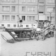 dzieci bawiące się na zbudowanej z drewnianych pali imitacji łodzi, tłem zdjęcia jest fragment bloku mieszkalnego z rzędami okien