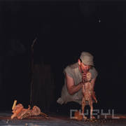 mężczyzna w siadzie klęcznym trzyma w rękach drewnianą lalkę chłopca, przed nimi rozsypane monety, z lewej leży drewniana lalka królika