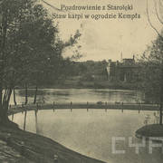 na pierwszym planie staw, na jego brzegach drzewa, w głębi z prawej fragment kratownicowego mostu