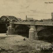 stalowy most na pięciu przęsłach i murowanych, masywnych filarach, na moście ozdobne latarnie, w głębi budynki, z prawej dwa wysokie kominy