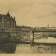 kratownicowy most nad rzeką, po lewej wysokie nabrzeże zabudowane kamienicami