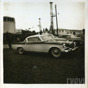 grupa osób przyglądająca się samochodom prezentowanym na placu targowym