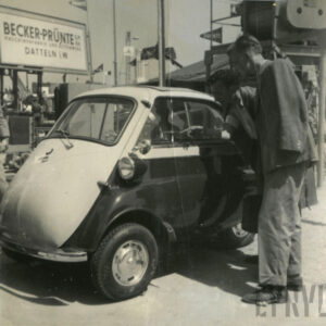dwóch mężczyzn ubranych w długie spodnie i marynarki przyglądających się mikrosamochodowi BMW Isetta