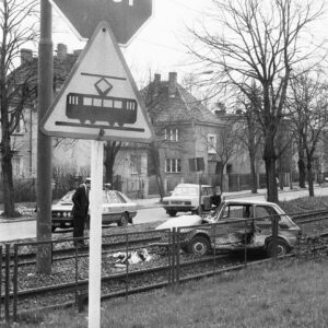 zniszczony samochód fiat 126p na torowisku tramwajowym na tle domów wolnostojących i drzew; na pierwszym planie znaki drogowe "uwaga tramwaj" i "stop"