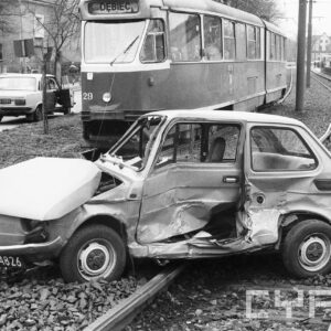 zniszczony samochód fiat 126p na torowisku tramwajowym na tle tramwaju linii nr 9 i domów wolnostojących