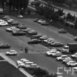 kilkanaście samochodów na placu otoczonym trawą i drzewami