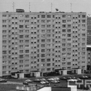 budynek z wielkiej płyty, przed nim trawnik oraz parking z samochodami