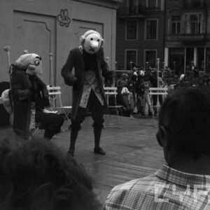 aktorzy w przebraniach występujący przed grupą ludzi na scenie ustawionej na tle zabytkowych kamienic