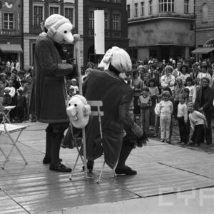 aktorzy w przebraniach występujący przed grupą ludzi na scenie ustawionej na tle zabytkowych kamienic