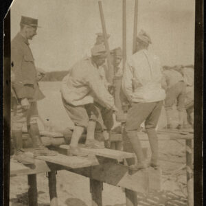 Grupa mężczyzn w roboczych strojach wojskowych pracująca przy budowie drewnianego mostu.