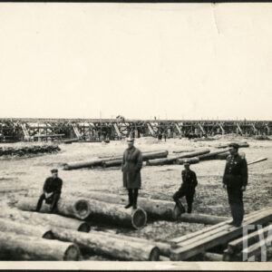 Czterech mężczyzn w mundurach wojskowych stojących przy drewnianych balach na tle mostu.