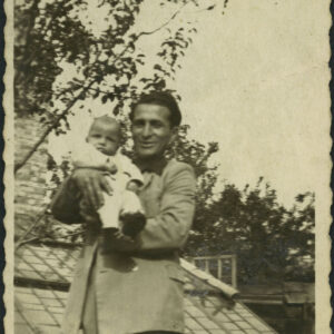 młody mężczyzna w marynarce trzymający na rękach niemowlaka, w głębi szklarnia