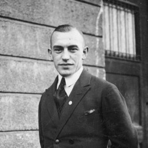 Mężczyzna w średnim wieku ubrany w garnitur stoi na tle murowanego budynku i drzwi.