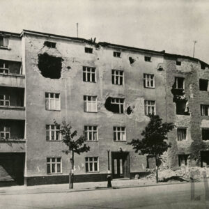 frontowa elewacja domu mieszkalnego z balkonami na narożniku i zrujnowanymi fragmentami po ostrzale