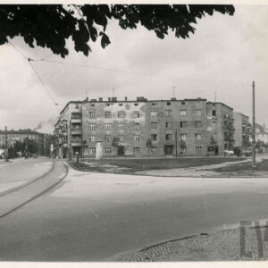 ulica z torami tramwajowymi, rozległy trawnik, w głębi domy mieszkalne