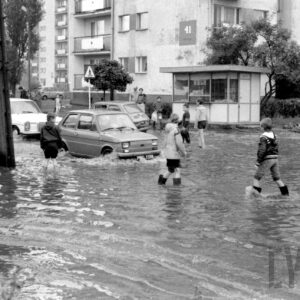 samochody na zalanej wodą ulicy pośród bloków