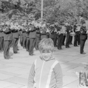 chłopiec na tle grupy mężczyzn w różnym w wieku ubranych w mundury górnicze, grających na różnych instrumentach muzycznych