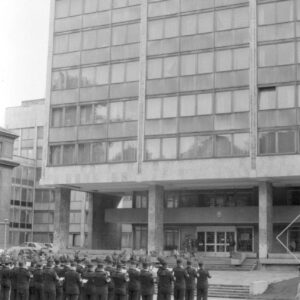 grupa mężczyzn w różnym w wieku ubrana w mundury górnicze, stojąca na tle przeszklonego wieżowca