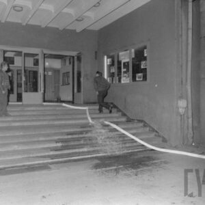 wąż strażacki leżący na schodach prowadzących do budynku, na schodach widać dwóch dorosłych mężczyzn