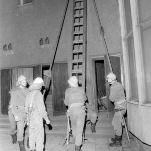 grupa strażaków przy drabinie opartej o budynek w czasie akcji gaśniczej 