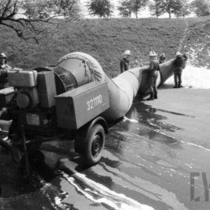 grupa mężczyzn w kombinezonach i hełmach strażackich stoi przy dużym wężu wypompowującym wodę