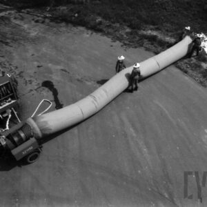 grupa mężczyzn w kombinezonach i hełmach strażackich stoi przy dużym wężu wypompowującym wodę