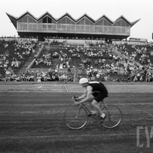 mężczyzna w stroju sportowym jadący na rowerze na tle kibiców siedzących na trybunach stadionu