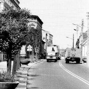 żyrafa w specjalnym samochodzie transportowym jadącym ulicą między kamienicami