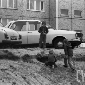 dzieci bawiące się na nasypie ziemnym na tle samochodów i budynku mieszkalnego z wielkiej płyty