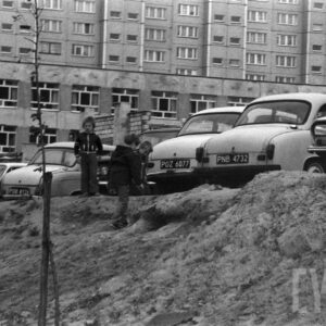 dzieci bawiące się na nasypie ziemnym na tle samochodów i budynku mieszkalnego z wielkiej płyty