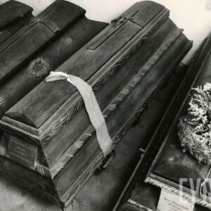 cztery drewniane trumny z krzyżami na wiekach, jedna z nich przepasana wstęgą, na kolejnej wiązanka kwiatów