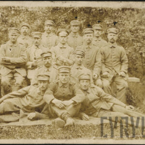 grupa młodych mężczyzn w mundurach wojskowych, dwóch leży bokiem na trawie, jeden siedzi na trawie, część siedzi na ławce, pozostali stoją