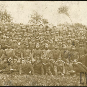 duża grupa młodych mężczyzn w mundurach wojskowych, dwóch klęczy na jednym kolanie, część leży bokiem na trawie, część siedzi, pozostali stoją