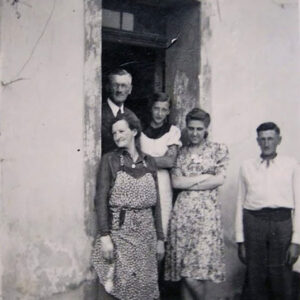 trzy kobiety stoją w środku, po bokach dwóch mężczyzn stoi w wejściu do murowanego budynku