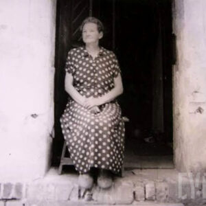 starsza kobieta siedzi na krześle w progu wejścia do murowanego budynku