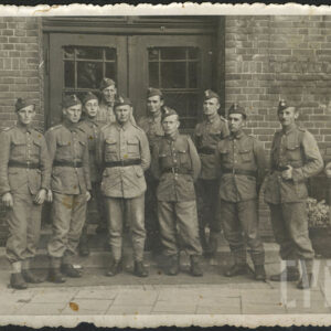 grupa mężczyzn w mundurach wojskowych na tle ceglanego budynku z drewnianymi drzwiami