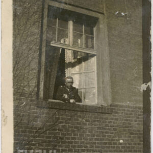 mężczyzna w mundurze wojskowym wyglądający przez okno budynku z cegieł