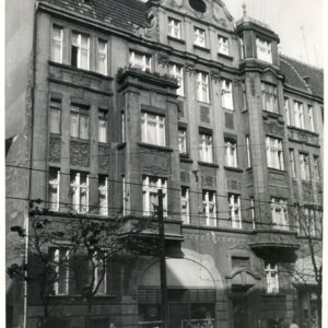 czteropiętrowa kamienica z poddaszem i ozdobnym szczytem oraz ze zdobieniami na fasadzie 