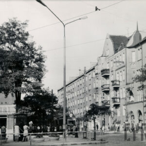 ulica, przy niej kilkupiętrowe kamienice i drzewa, spacerują ludzie