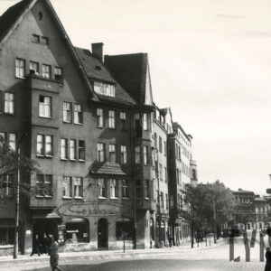 trzypiętrowa kamienica z zamieszkałym poddaszem, brukowana ulica, spacerujący ludzie