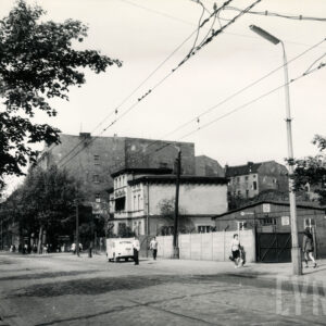brukowana ulica z torami tramwajowymi, pośrodku dwupiętrowa willa, z prawej drewniany barak