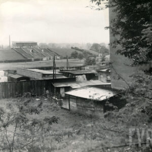 zdjęcie wykonane między budynkami, poniżej widoczne baraki, w głębi trybuna stadionu