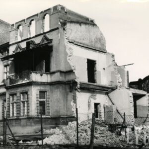 trzykondygnacyjny budynek z częściowo wyburzonymi ścianami, przy nim leży gruz