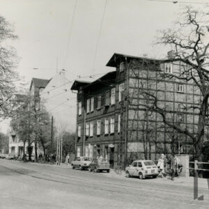 asfaltowa ulica, przy niej zaparkowane samochody, wzdłuż ulicy kilkupiętrowe kamienice