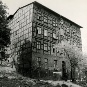 trzypiętrowy budynek o konstrukcji szkieletowej, drewnianej, wypełnionej cegłami, stoi na skarpie