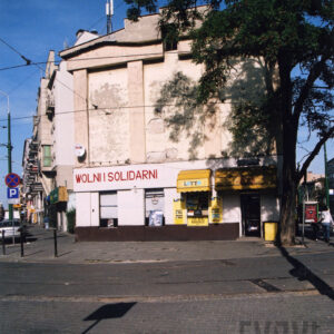 murowana ściana bez okien, z odpadającym tynkiem, w paśmie parteru okna sklepu