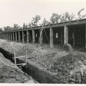 murowany, długi budynek z przedzielonymi boksami w trakcie budowy, przed budynkiem gruz i wykopany wał