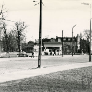 brukowana ulica, w głębi kiosk z gazetami, za nim stacja benzynowa, w głębi kamienice