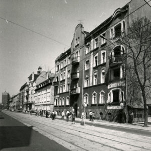 asfaltowa ulica z torami tramwajowymi, przy niej kilkupiętrowe kamienice